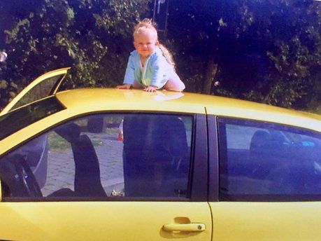 Dochter Britt bij de gele lesauto van Autorijschool Hartkamp, eind 2003